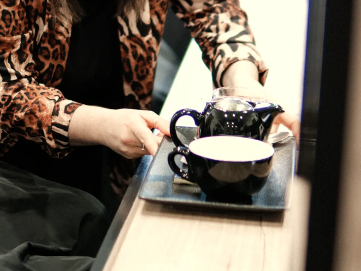 A stylist placing a tray with a pot of tea and a cup beside a guest in the chair